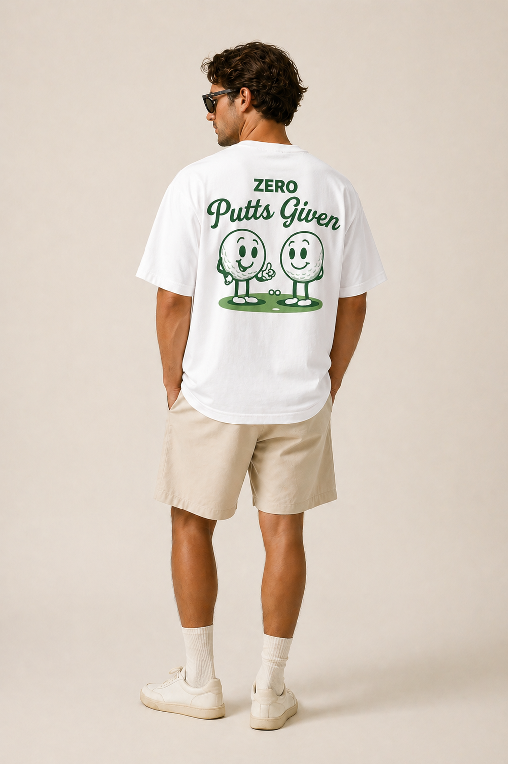 Man wearing a white t-shirt with 'Zero Putts Given' graphic on the back, standing against a beige background.